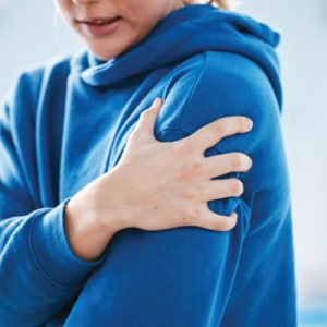Person gripping their shoulder to show shoulder pain and restricted movement.